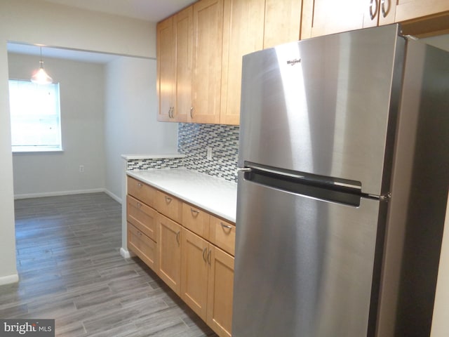 kitchen with light wood finished floors, freestanding refrigerator, baseboards, backsplash, and light countertops