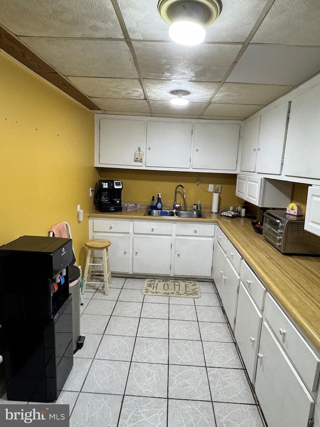 kitchen with a toaster, light tile patterned floors, a sink, light countertops, and white cabinets