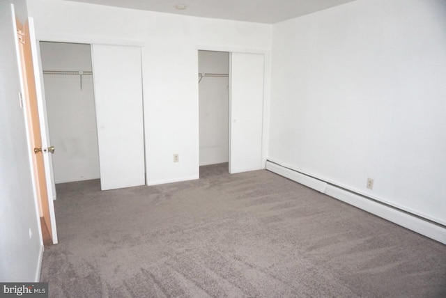 unfurnished bedroom with baseboard heating, carpet flooring, and multiple closets