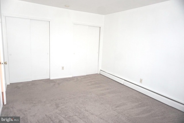 unfurnished bedroom featuring baseboard heating, carpet, and two closets