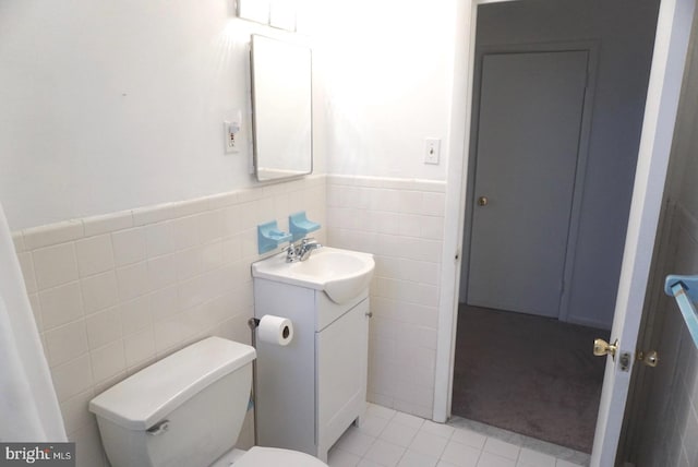 bathroom with tile walls, vanity, toilet, a wainscoted wall, and tile patterned floors