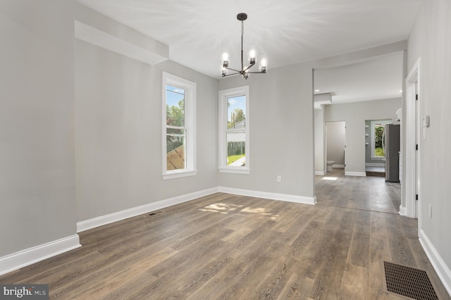 unfurnished dining area featuring a healthy amount of sunlight, an inviting chandelier, visible vents, and wood finished floors