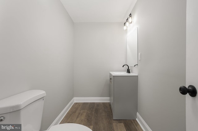 half bath with vanity, toilet, wood finished floors, and baseboards