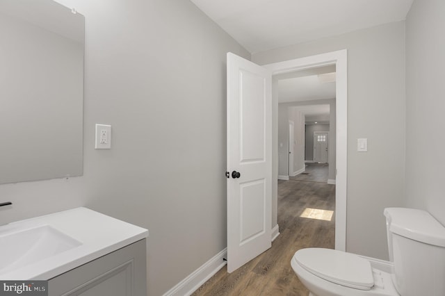 half bathroom featuring toilet, baseboards, wood finished floors, and vanity