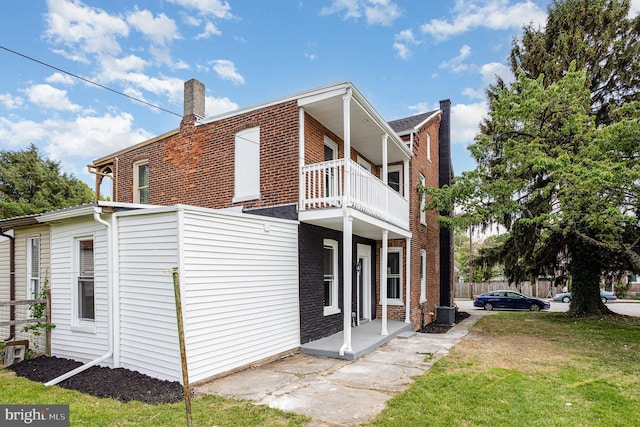 exterior space with a balcony, a chimney, a lawn, brick siding, and fence
