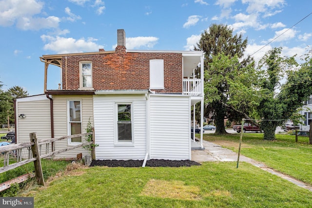 back of house with a balcony, fence, a chimney, and a lawn