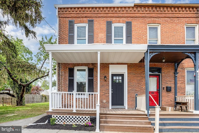 townhome / multi-family property featuring brick siding, covered porch, and fence