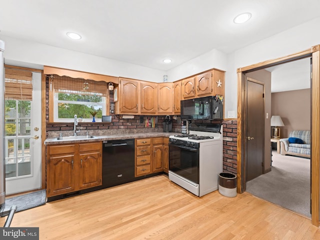 kitchen featuring a sink, brown cabinetry, black appliances, light wood finished floors, and backsplash