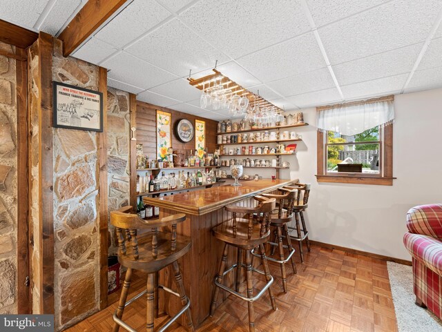 bar featuring a bar, baseboards, and a drop ceiling