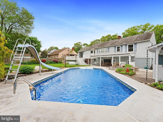 pool featuring a water slide, a deck, fence, a patio area, and stairs
