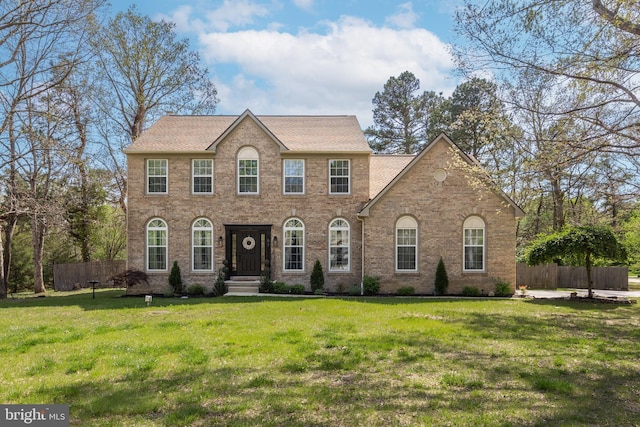 colonial home with fence, a shingled roof, brick siding, and a front yard