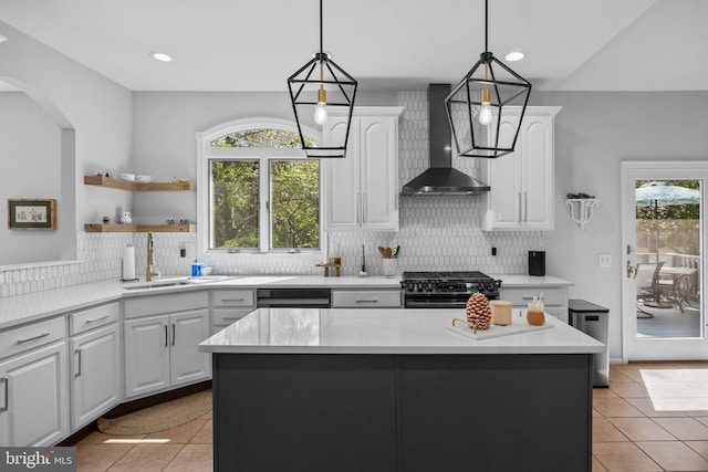 kitchen featuring light tile patterned floors, a sink, gas range oven, wall chimney exhaust hood, and white cabinetry