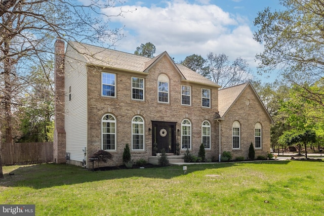 colonial-style house with brick siding, a chimney, fence, and a front yard