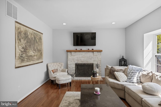 living room featuring wood finished floors, a brick fireplace, visible vents, baseboards, and recessed lighting