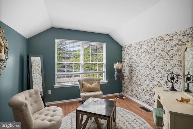 living area featuring lofted ceiling, wallpapered walls, baseboards, visible vents, and wood finished floors