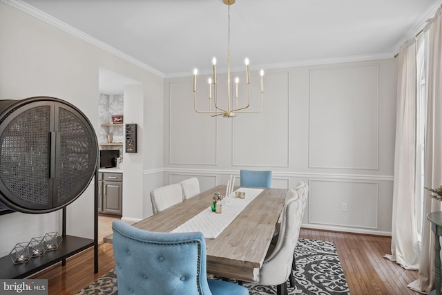 dining space featuring ornamental molding, a decorative wall, wood-type flooring, and a notable chandelier