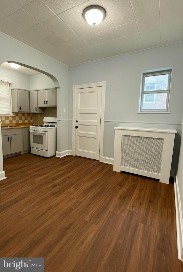 kitchen with white gas stove, dark wood finished floors, arched walkways, backsplash, and radiator heating unit