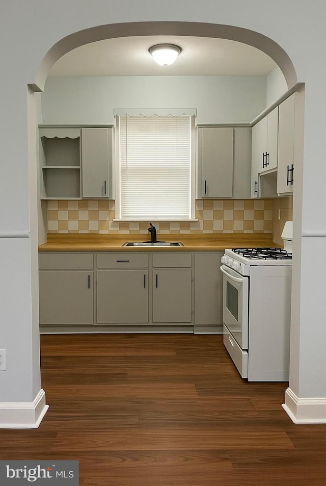 kitchen featuring arched walkways, decorative backsplash, gas range gas stove, and a sink