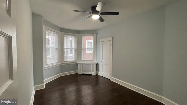 spare room with a ceiling fan, dark wood-style flooring, and baseboards