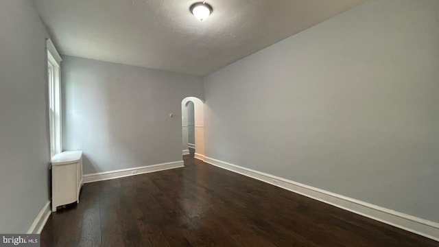 empty room featuring dark wood-style flooring, baseboards, and arched walkways