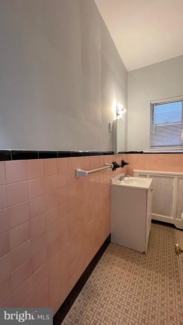 bathroom featuring vanity, radiator, tile walls, and wainscoting