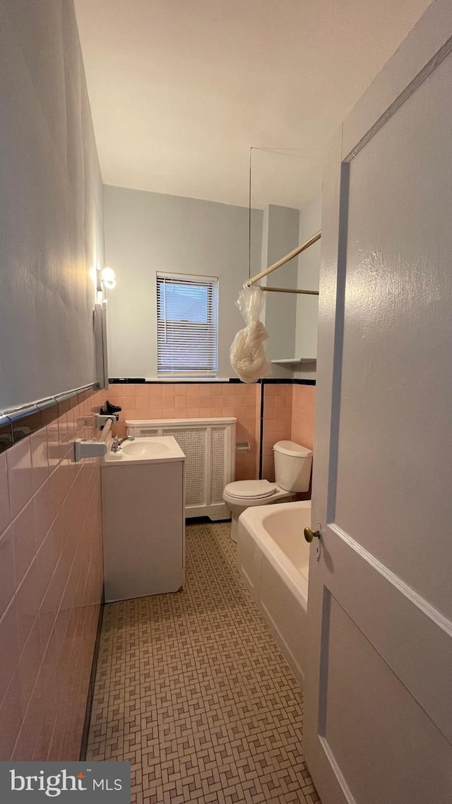 bathroom featuring tile walls, toilet, wainscoting, tile patterned floors, and a bathing tub