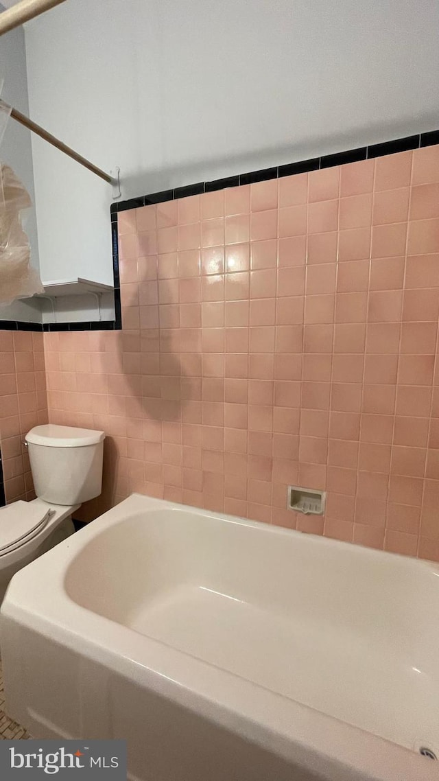 full bath with toilet, tile walls, and a bathtub