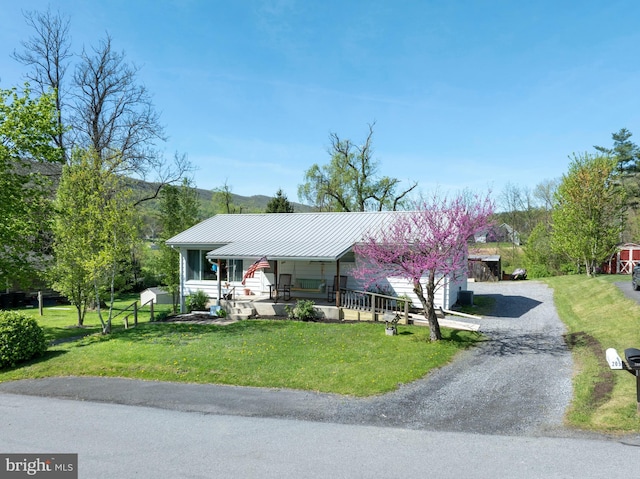 view of front of home with a porch, a front yard, metal roof, gravel driveway, and a standing seam roof