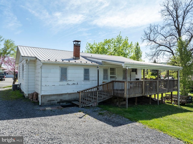 back of house with a chimney, metal roof, a deck, a lawn, and cooling unit