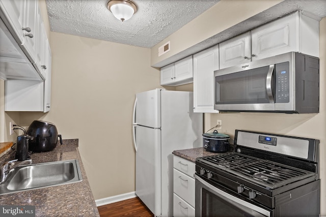 kitchen with stainless steel appliances, a sink, dark countertops, white cabinetry, and baseboards