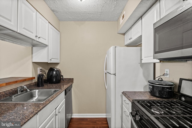 kitchen featuring appliances with stainless steel finishes, a sink, dark countertops, white cabinets, and a textured ceiling