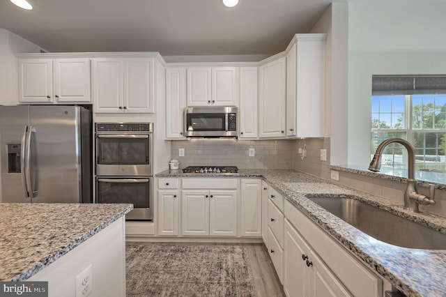 kitchen with a sink, stainless steel appliances, white cabinetry, decorative backsplash, and light stone counters