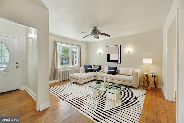 living room featuring radiator, light wood-style floors, a ceiling fan, and baseboards