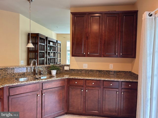 kitchen featuring a sink, dark stone counters, reddish brown cabinets, and decorative light fixtures