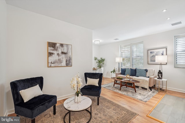 living area featuring a healthy amount of sunlight, baseboards, visible vents, and wood finished floors