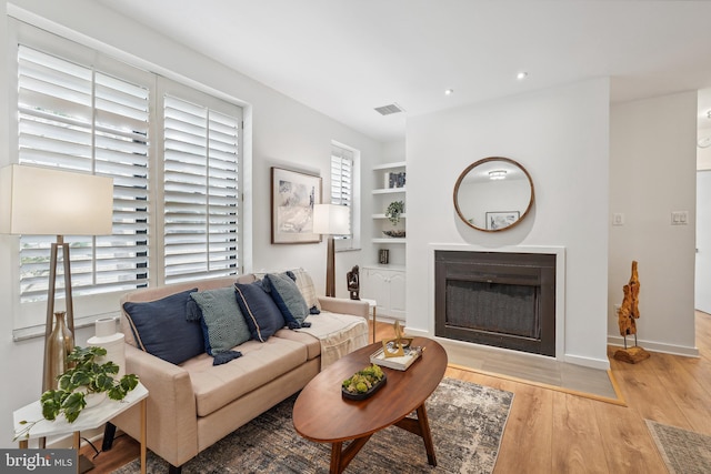 living area with baseboards, visible vents, built in features, wood finished floors, and a fireplace
