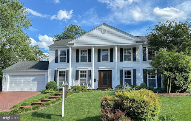 greek revival inspired property with a front yard, a porch, an attached garage, and decorative driveway