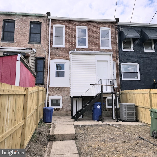back of property with brick siding, a fenced backyard, and central AC