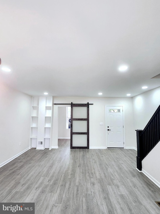 basement with baseboards, stairs, light wood finished floors, and a barn door