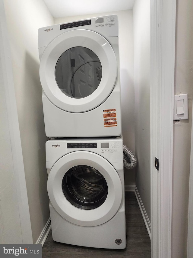 laundry area with stacked washer / dryer, baseboards, and wood finished floors