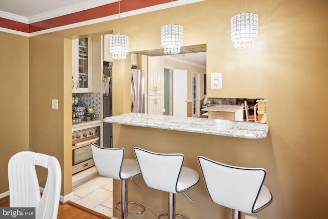 kitchen with a peninsula, a breakfast bar, crown molding, appliances with stainless steel finishes, and a chandelier