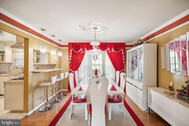 dining space featuring light wood-style flooring, ornamental molding, and a notable chandelier