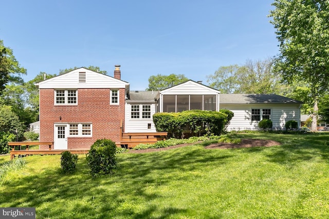 rear view of house featuring a sunroom, brick siding, a chimney, a yard, and a deck
