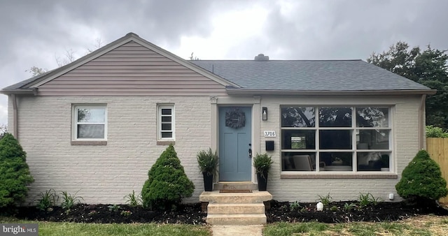 view of front of house featuring roof with shingles, fence, and brick siding