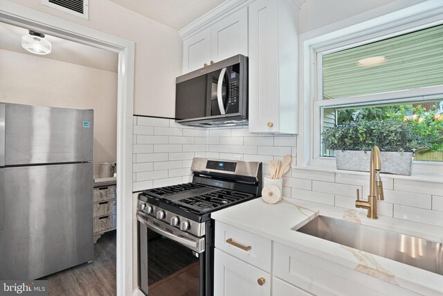 kitchen with stainless steel appliances, a sink, white cabinetry, and tasteful backsplash