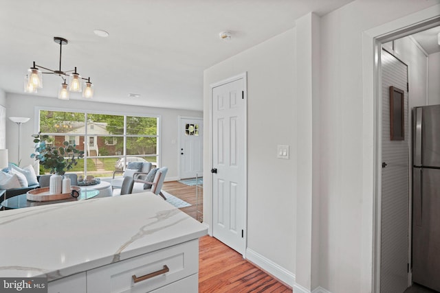 kitchen featuring freestanding refrigerator, light wood-type flooring, decorative light fixtures, baseboards, and white cabinetry