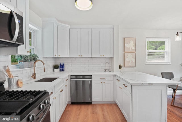 kitchen featuring appliances with stainless steel finishes, a peninsula, a sink, backsplash, and light wood-type flooring