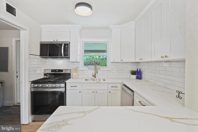 kitchen with appliances with stainless steel finishes, a sink, light stone counters, and white cabinets