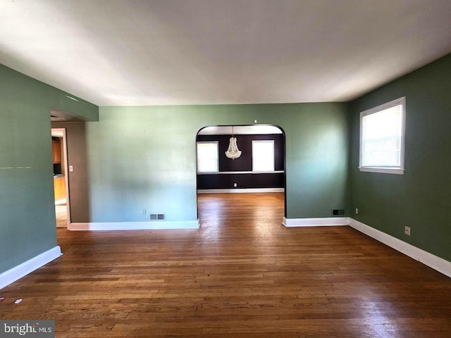 empty room featuring arched walkways, visible vents, plenty of natural light, and wood finished floors