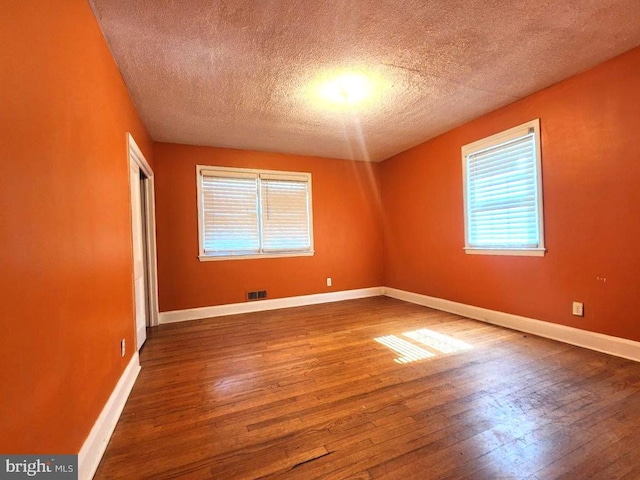 spare room featuring plenty of natural light, a textured ceiling, visible vents, and hardwood / wood-style floors